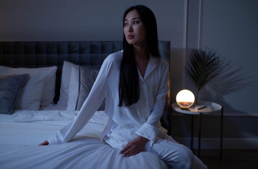 Woman in white pajamas sitting on a bed with warm lighting, showcasing a calm evening indoors.