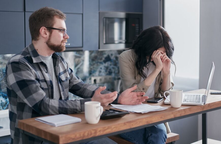 A couple seated at a table, looking stressed while discussing financial issues indoors.