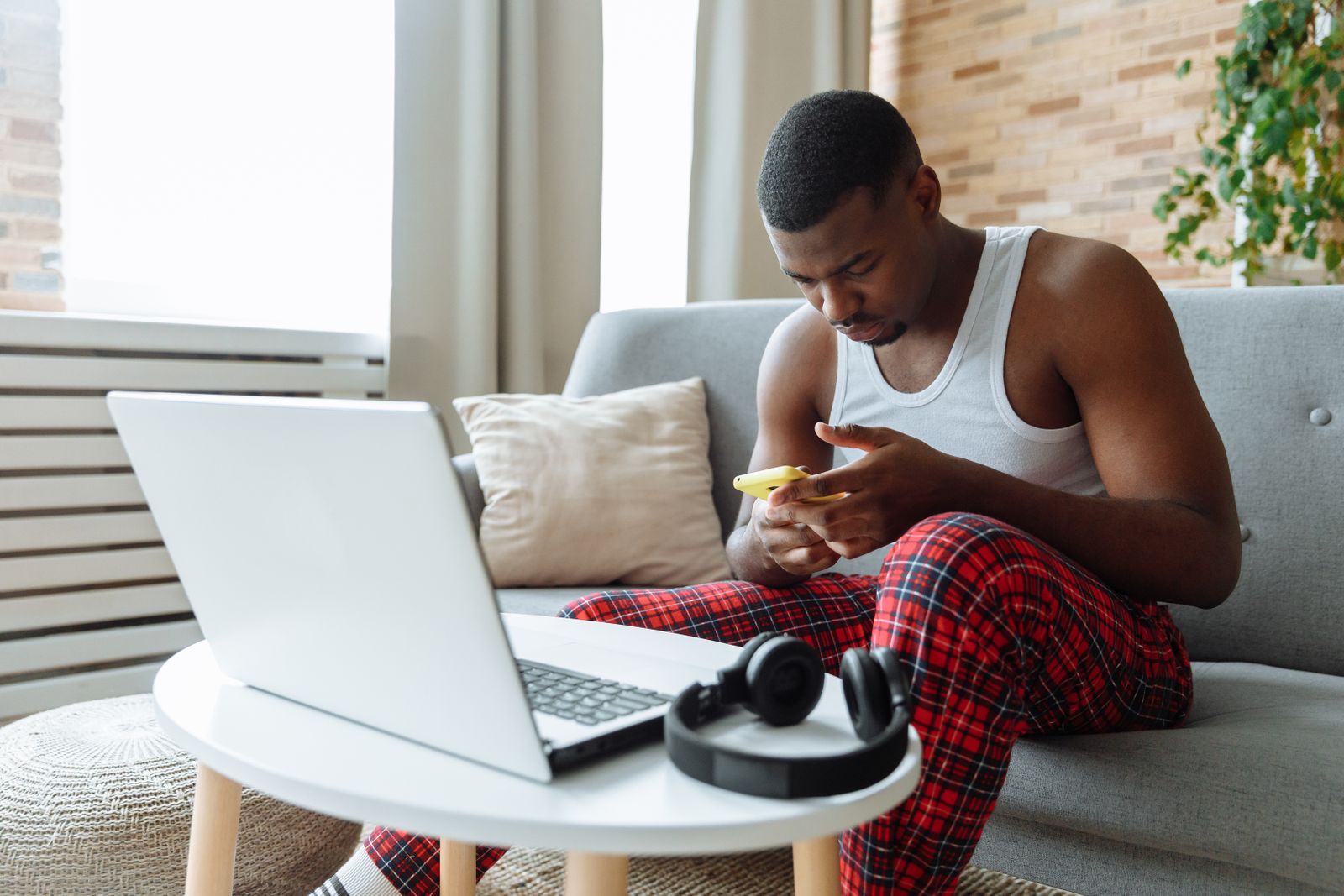 Man sitting on sofa, multitasking with laptop and smartphone in cozy living room.