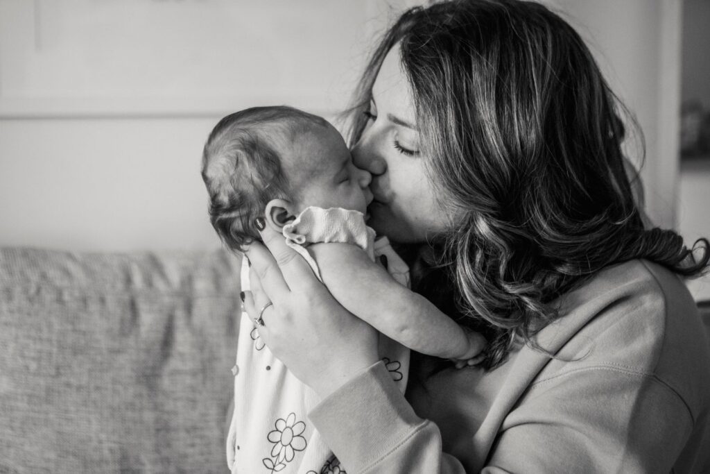A mother lovingly kisses her newborn in a warm, intimate moment.