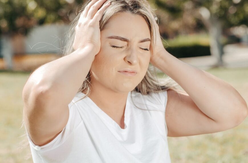 A woman outdoors holds her head, depicting stress or a headache.