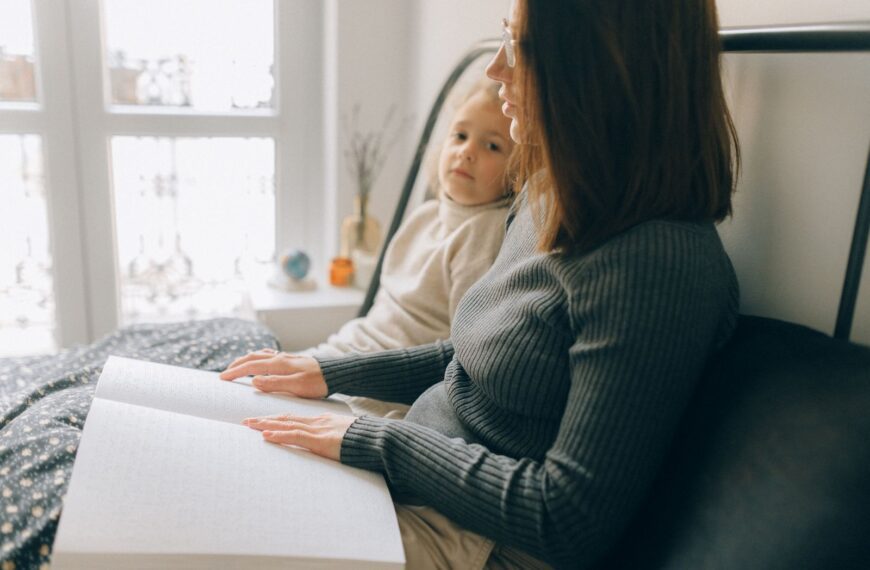 A woman and child reading a braille book in a cozy bedroom setting, enhancing child development.