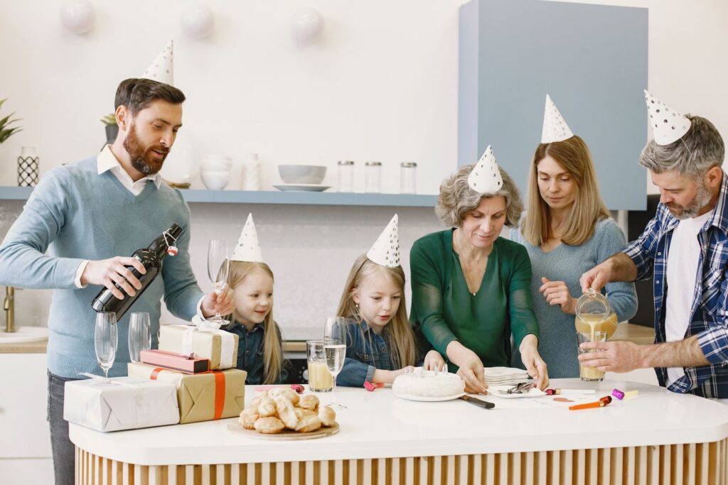 Family celebrating a birthday indoors with cake, party hats, gifts, and drinks.