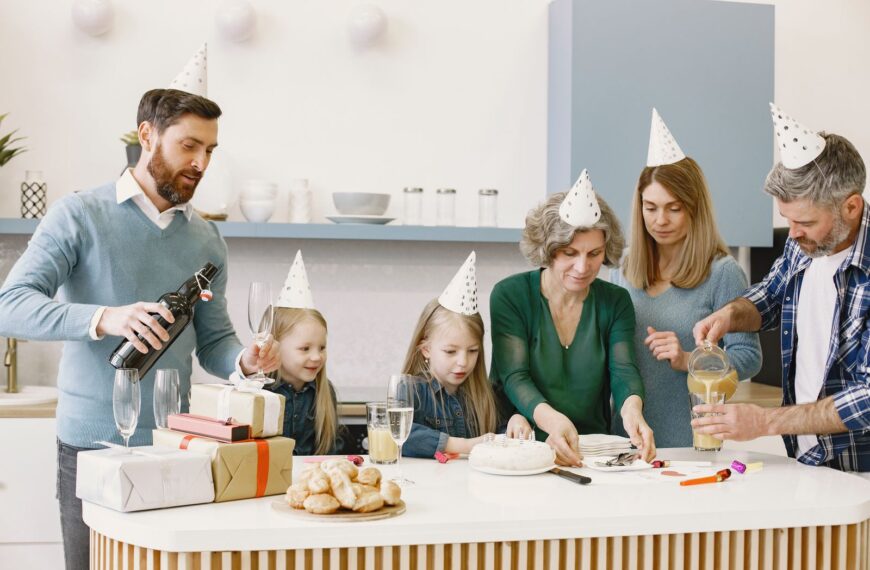 Family celebrating a birthday indoors with cake, party hats, gifts, and drinks.