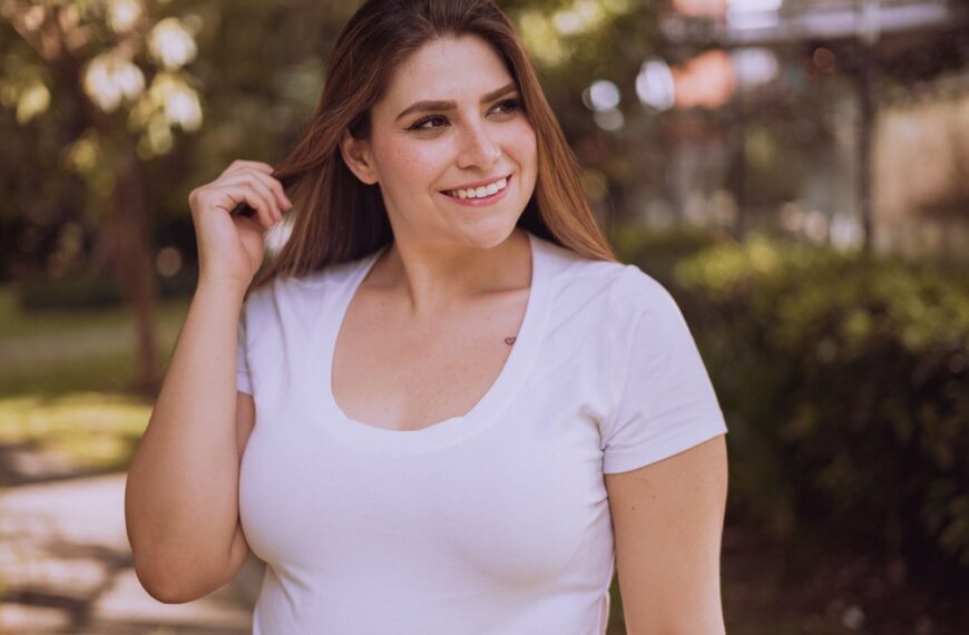 A woman smiles while posing in a white shirt outdoors during the day.