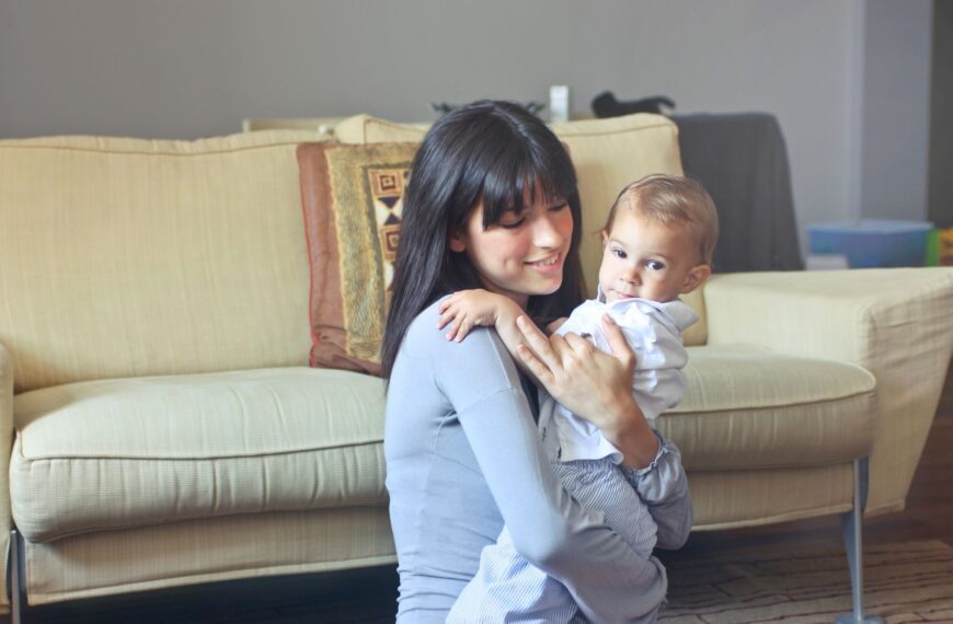 A mother lovingly embraces her baby indoors on a comfortable sofa capturing warmth and togetherness.