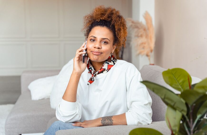 Young woman smiling while talking on the phone, sitting comfortably on a couch indoors.