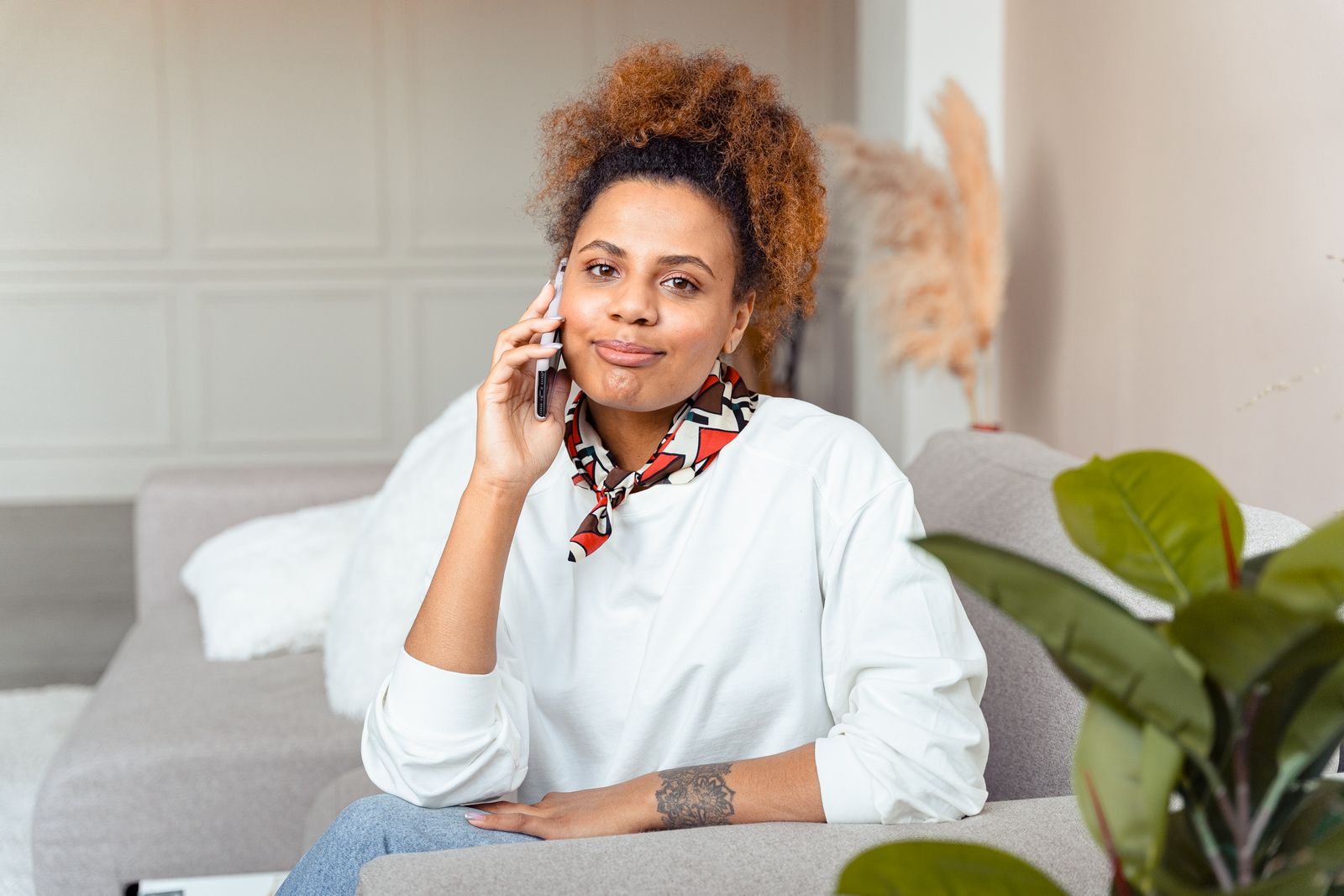 Young woman smiling while talking on the phone, sitting comfortably on a couch indoors.