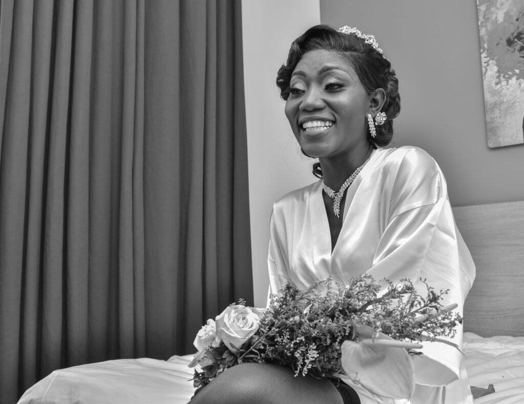 Black and white portrait of a smiling bride in a robe holding flowers.