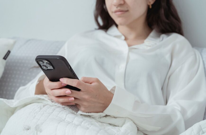 Young woman relaxing in bed while using a smartphone, enjoying leisure time indoors.