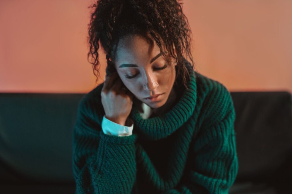 Contemplative African American woman in a green sweater, exuding calm and introspection, indoor setting.