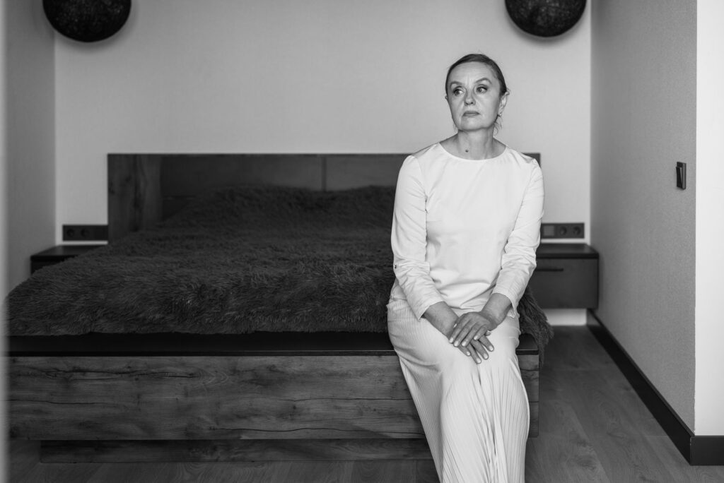 Black and white photo of a woman sitting in a modern bedroom with thoughtful expression.