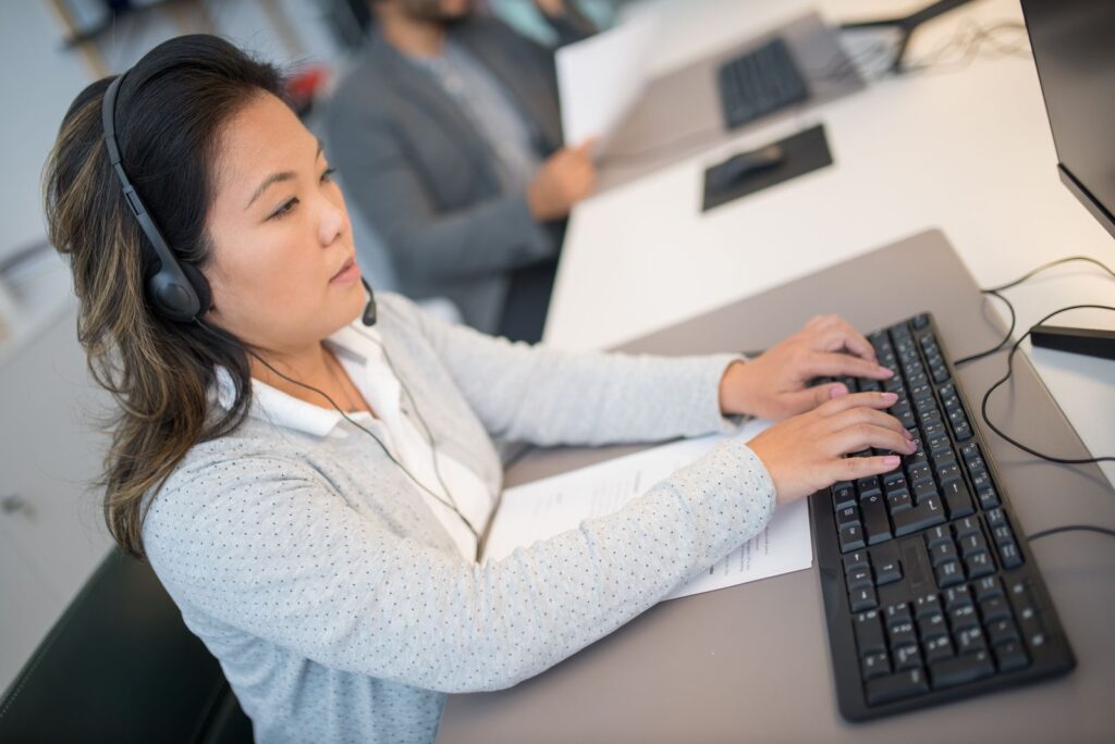 Asian woman working at a computer with headphones in a modern office setting.