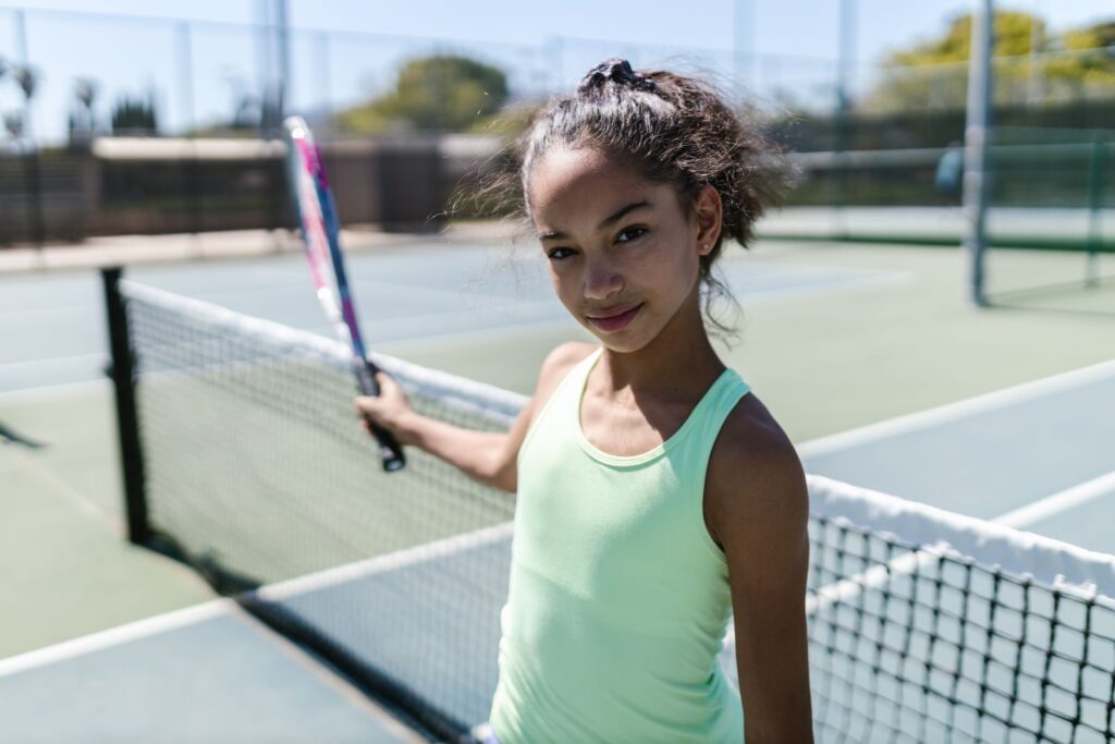Energetic teen girl smiling while playing tennis on a sunny day.
