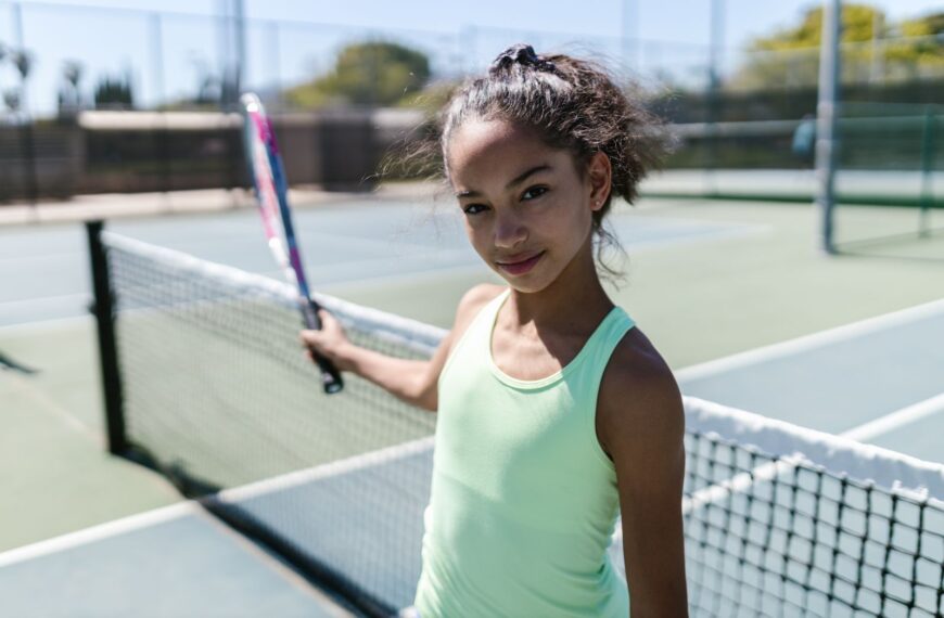 Energetic teen girl smiling while playing tennis on a sunny day.