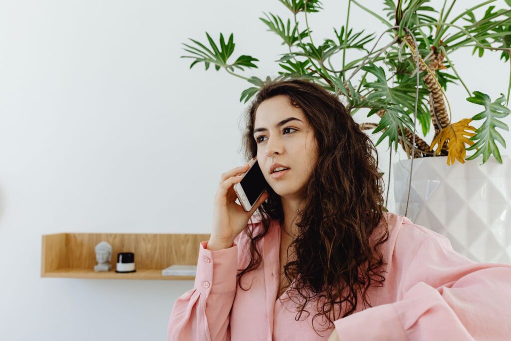 Confident young woman talking on smartphone in a modern interior with green plant background.
