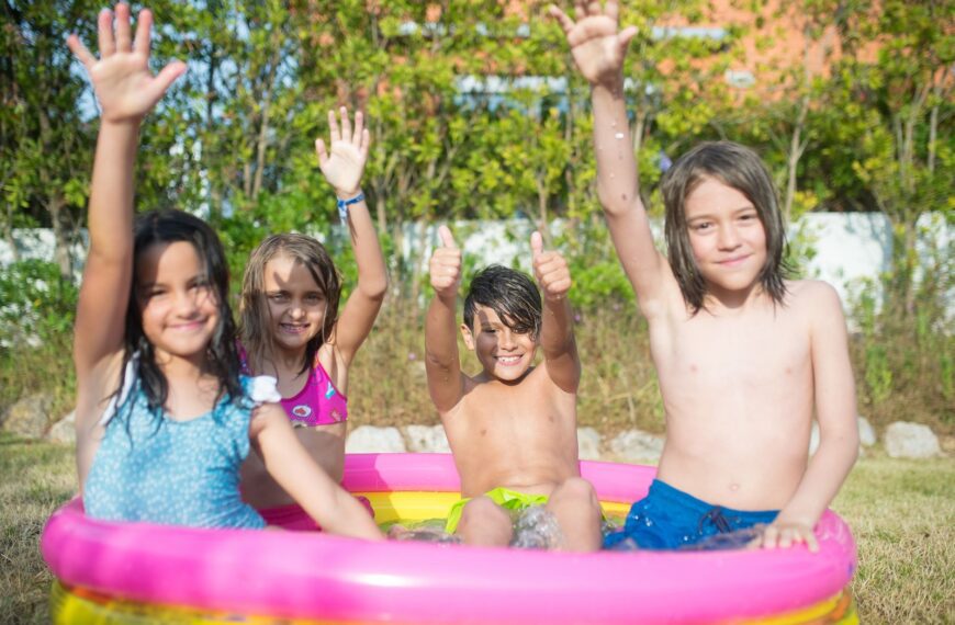 Children having fun in an inflatable pool outdoors, celebrating summer with laughter and raised arms.