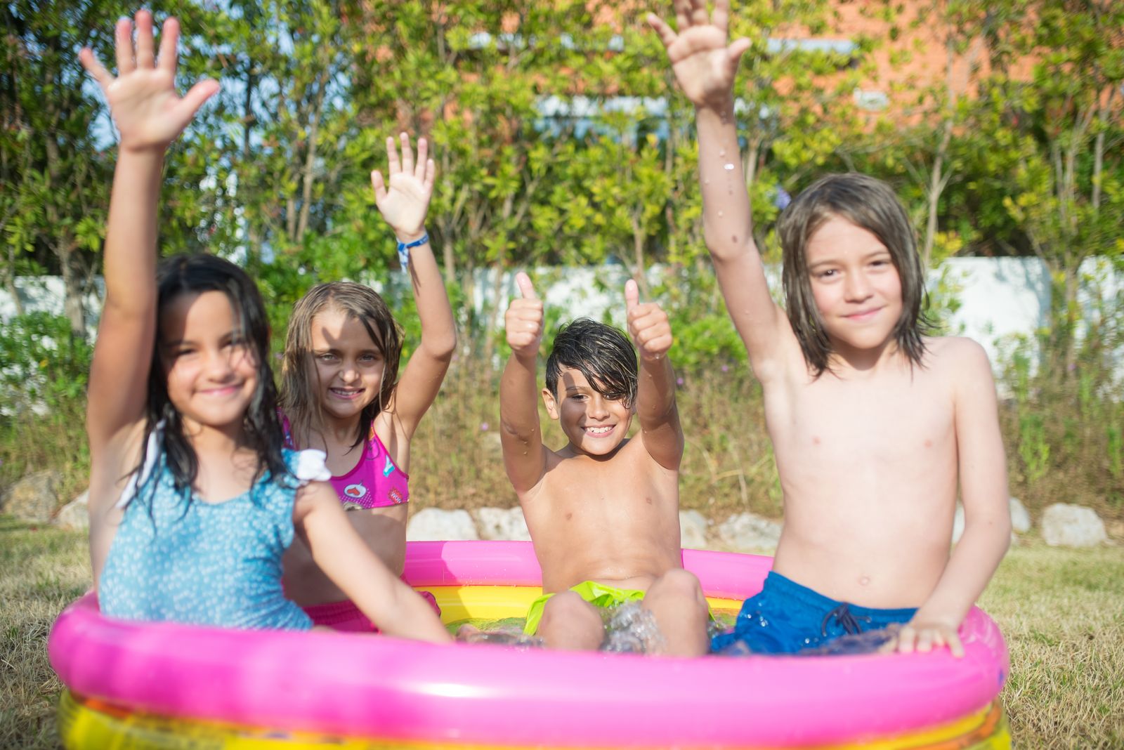 Children having fun in an inflatable pool outdoors, celebrating summer with laughter and raised arms.