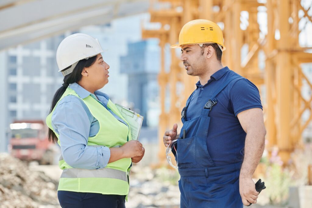 Two engineers wearing hard hats discuss project plans at a construction site.