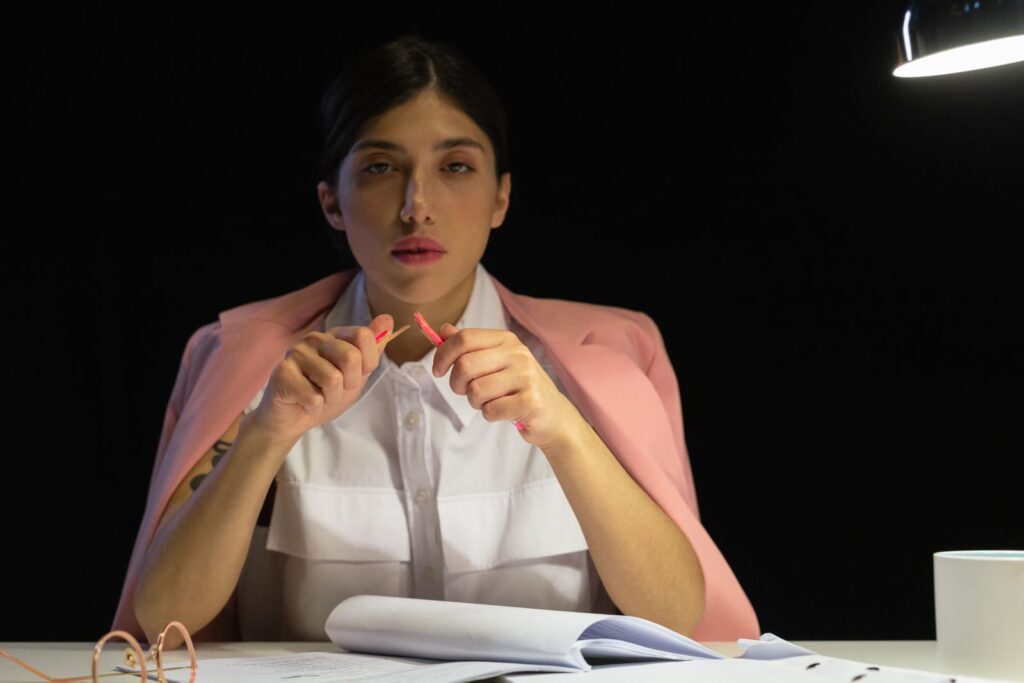 Woman in pink blazer sitting at a desk with papers under lamp light.