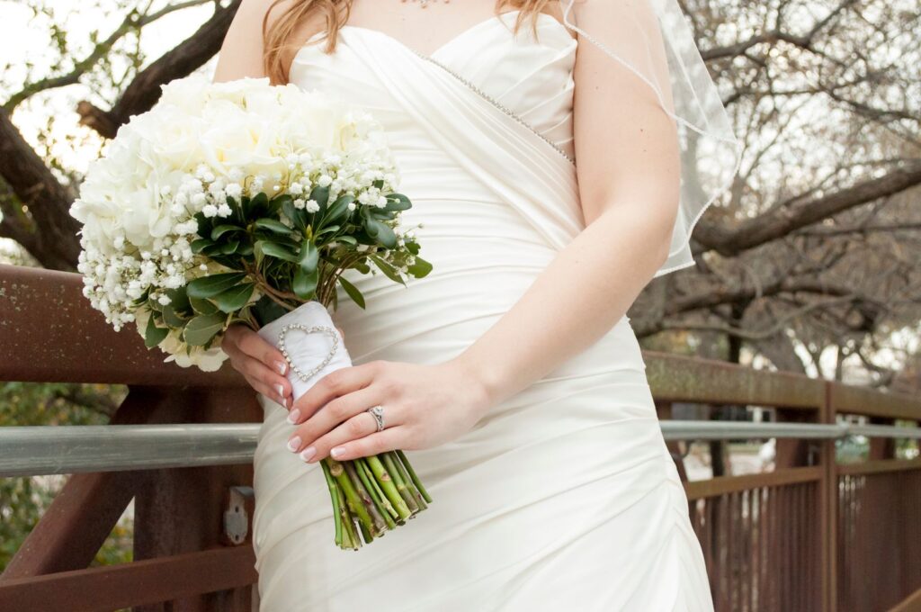 Close-up of a bride holding a white floral bouquet against a rustic bridge background.