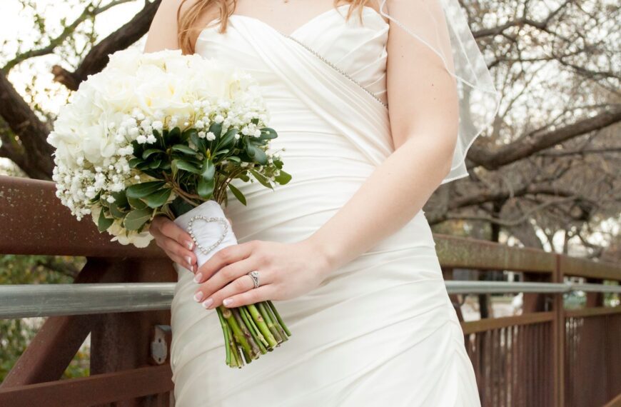 Close-up of a bride holding a white floral bouquet against a rustic bridge background.