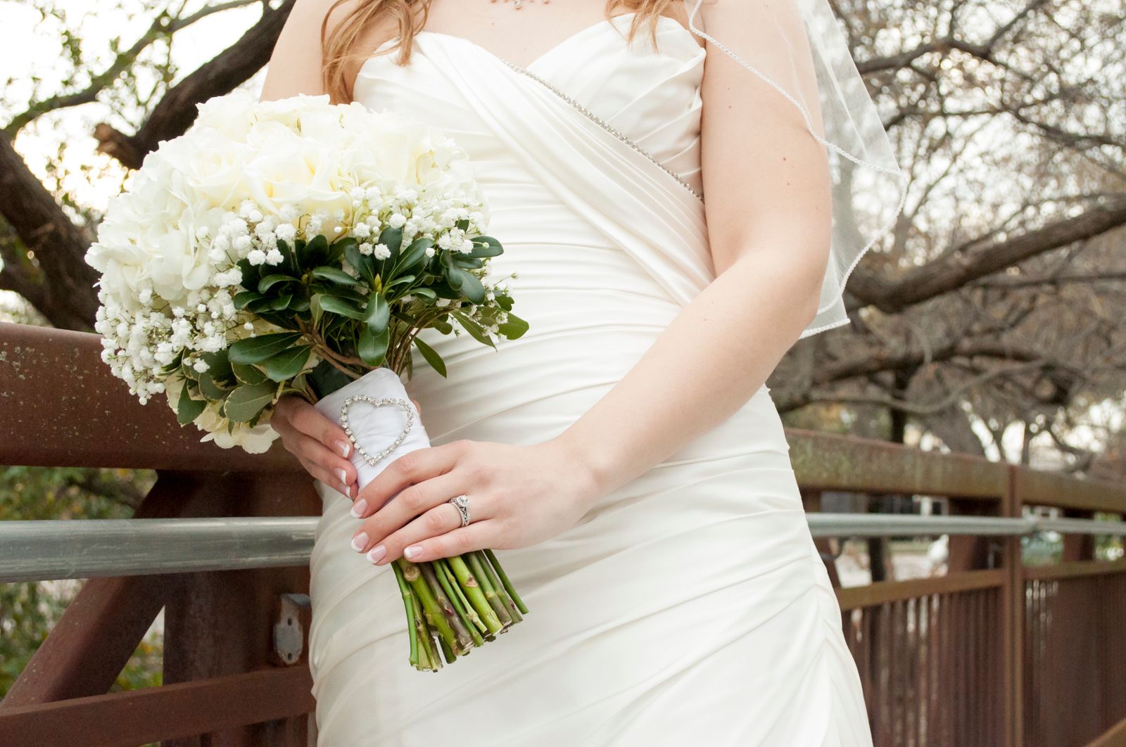 Close-up of a bride holding a white floral bouquet against a rustic bridge background.