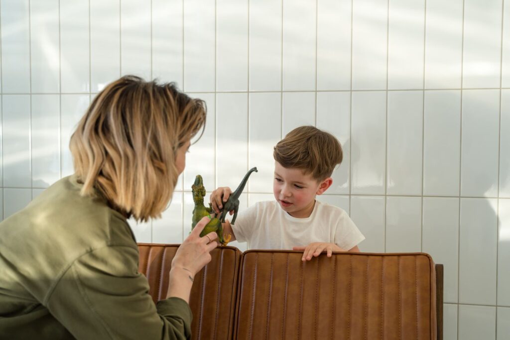 A mother and her young son enjoy playing with dinosaur toys in a sunlit room.