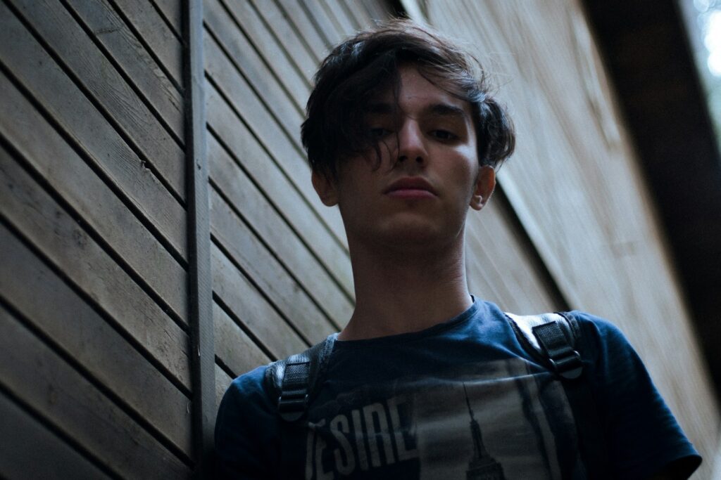 a young man leaning against a wooden wall