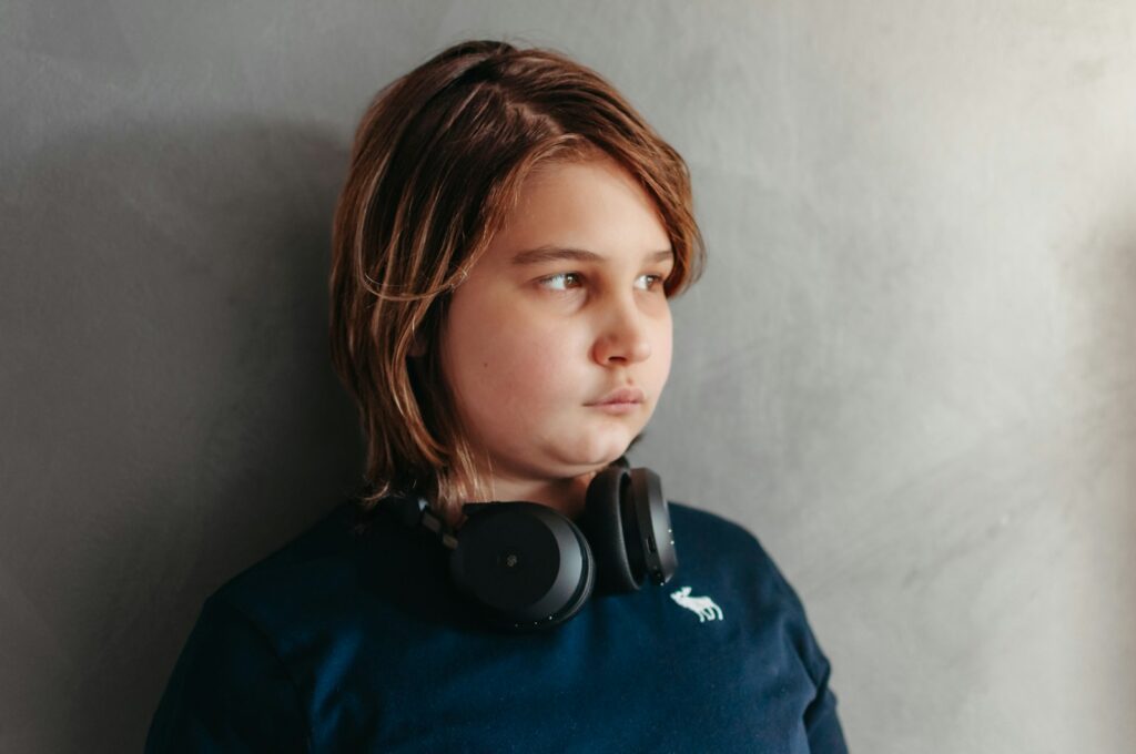 A boy with headphones looks thoughtfully away.