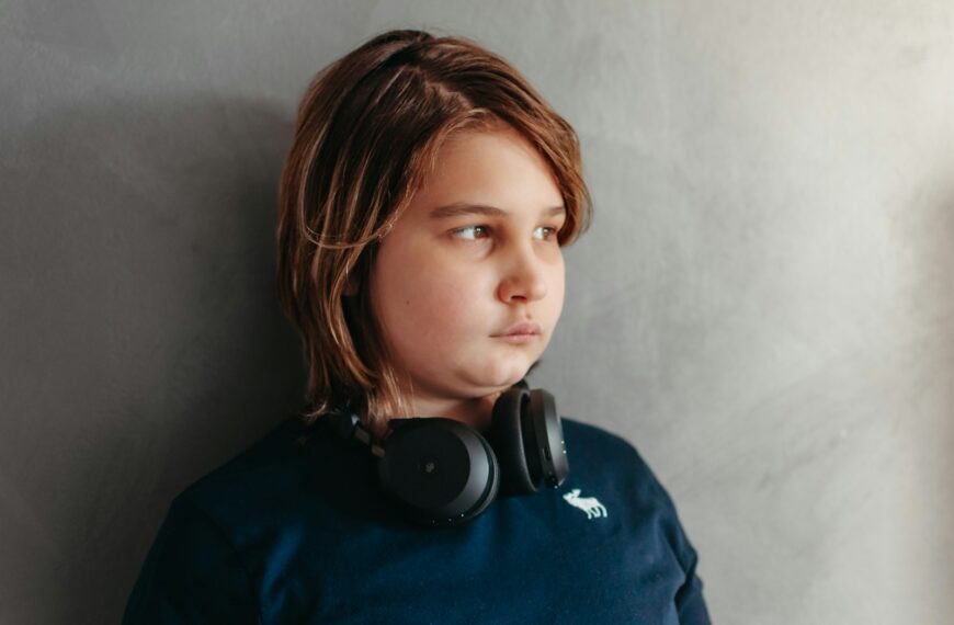 A boy with headphones looks thoughtfully away.
