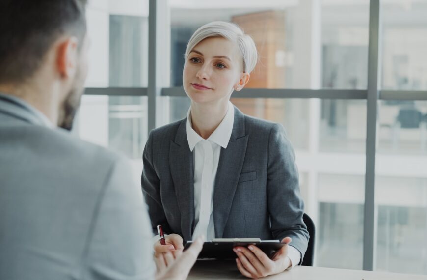 Woman in suit interviews man at desk