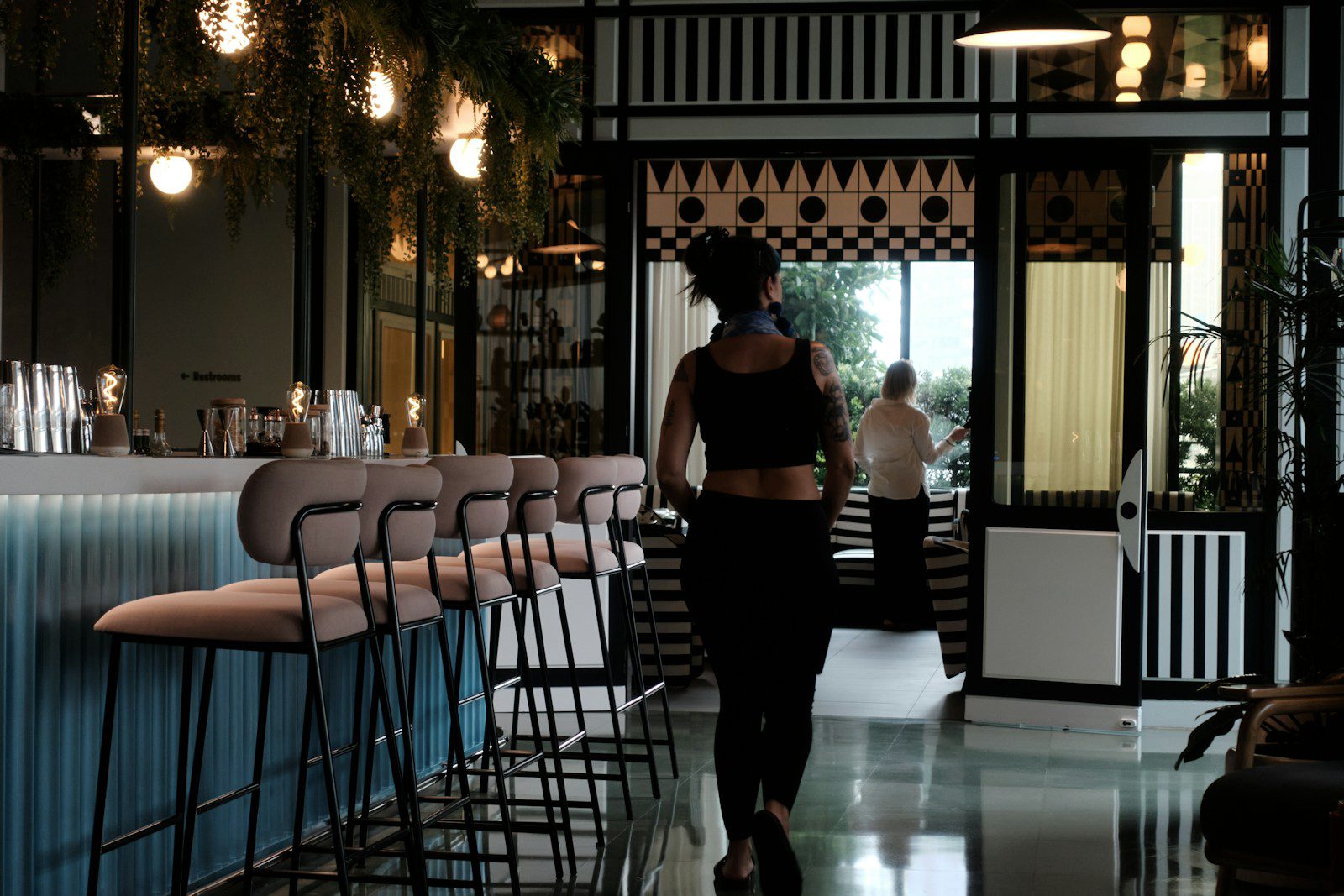 Woman walks into a stylish bar with stools.