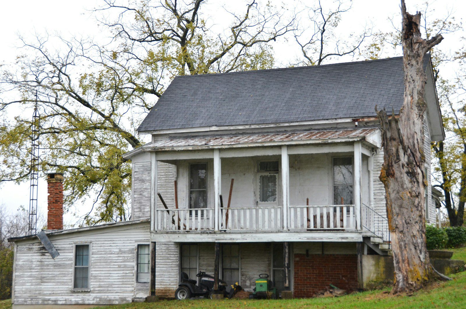 Old farmhouse with peeling paint and a large tree.