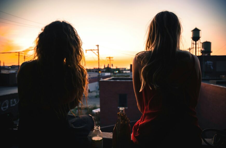 two women sitting on rooftop while watching sunset