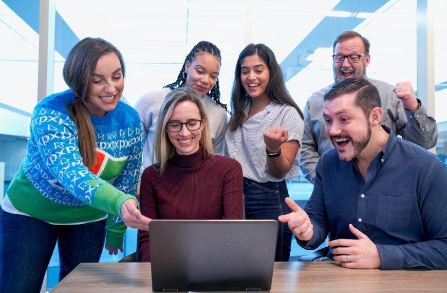 men and women sitting and standing while staring at laptop