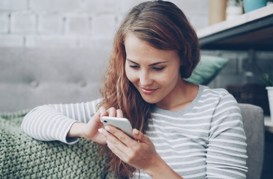 A young woman smiling while looking at her phone.