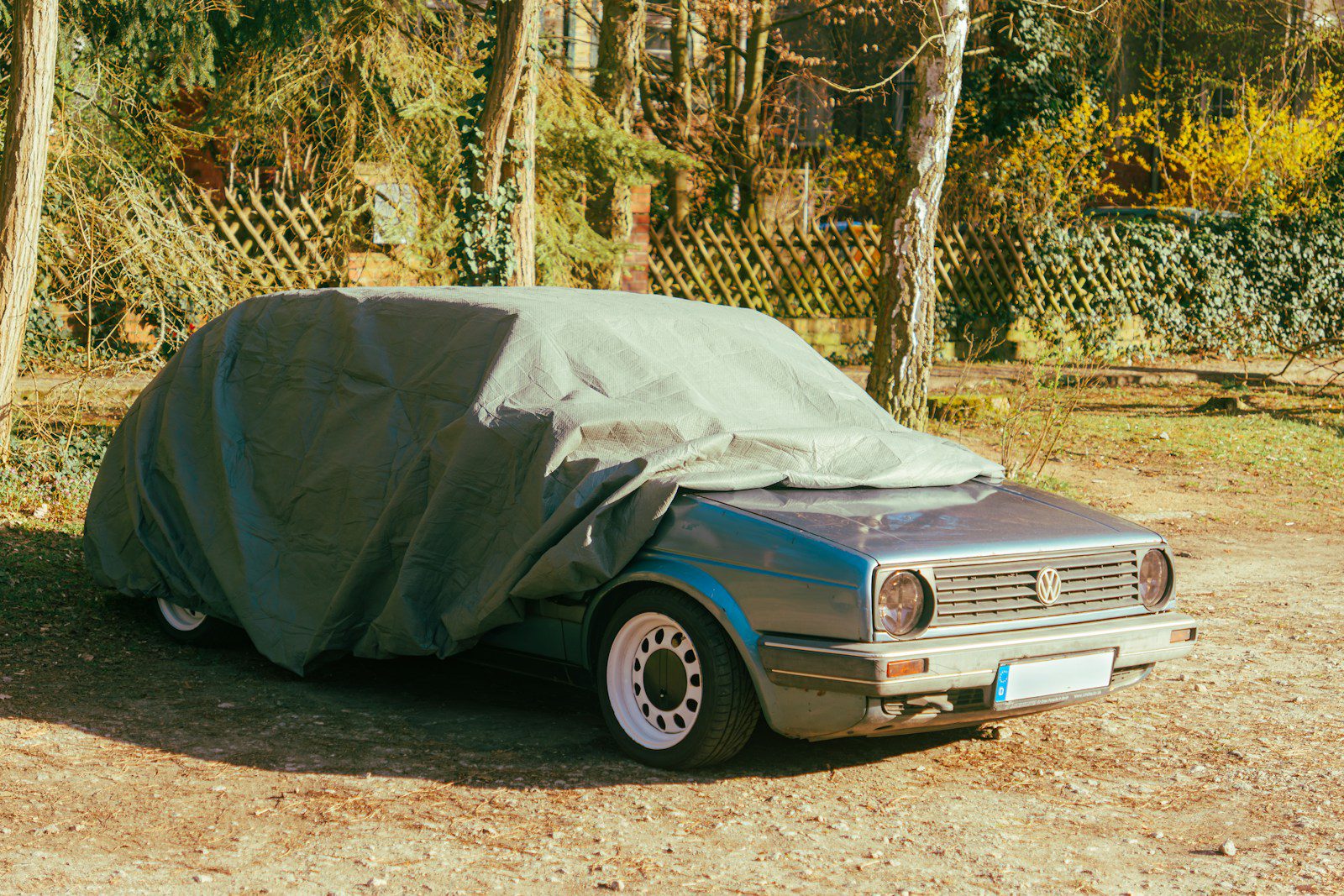 Car covered with a tarp in a wooded area.