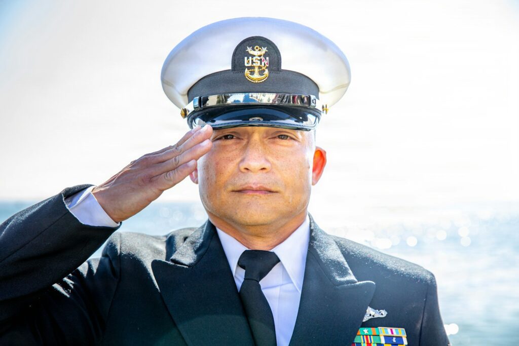A man in a us navy uniform salutes outdoors.