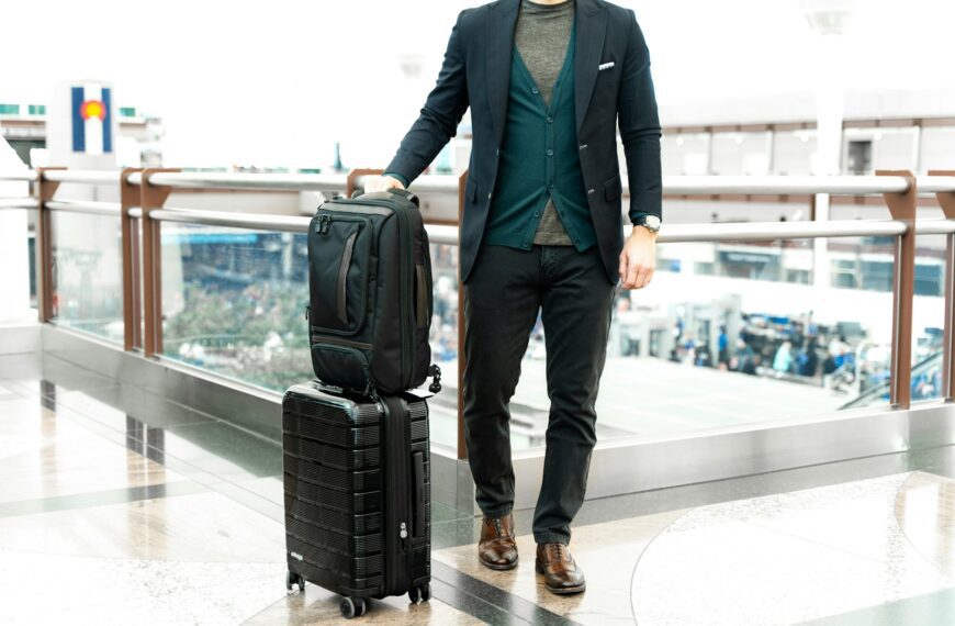 man in blue suit jacket and black pants standing beside black luggage bag