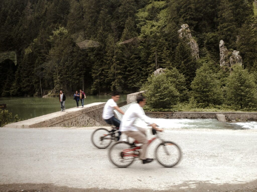 a couple of men riding bikes on a road by a river
