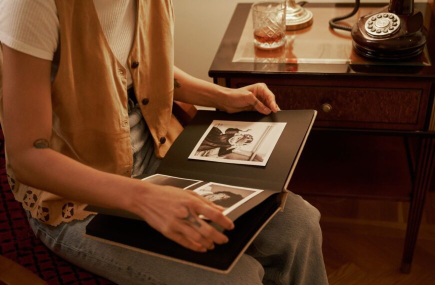 A woman sitting indoors, browsing a vintage photo album with a retro telephone beside her.