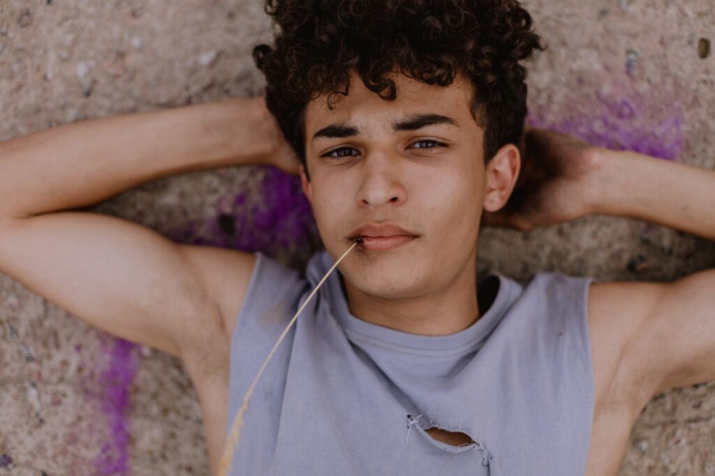 Teenager with curly hair lying on the ground, casual and contemplative mood.