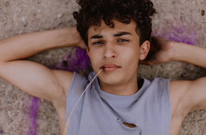Teenager with curly hair lying on the ground, casual and contemplative mood.