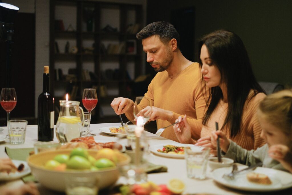 A family gathered around a dinner table indoors, enjoying a meal together with wine and candles.