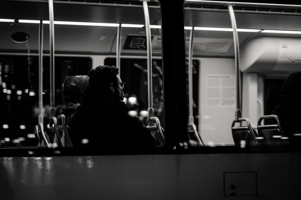 Grayscale image of passengers sitting inside a bus at night, viewed from outside.