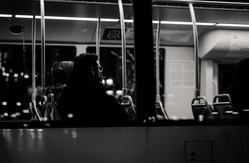 Grayscale image of passengers sitting inside a bus at night, viewed from outside.