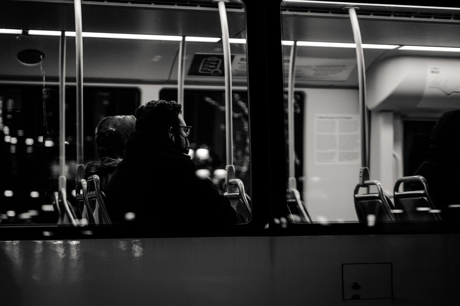Grayscale image of passengers sitting inside a bus at night, viewed from outside.