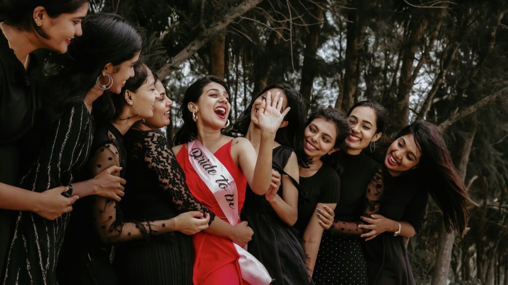 A group of women joyously celebrating outdoors with the bride-to-be wearing a sash.