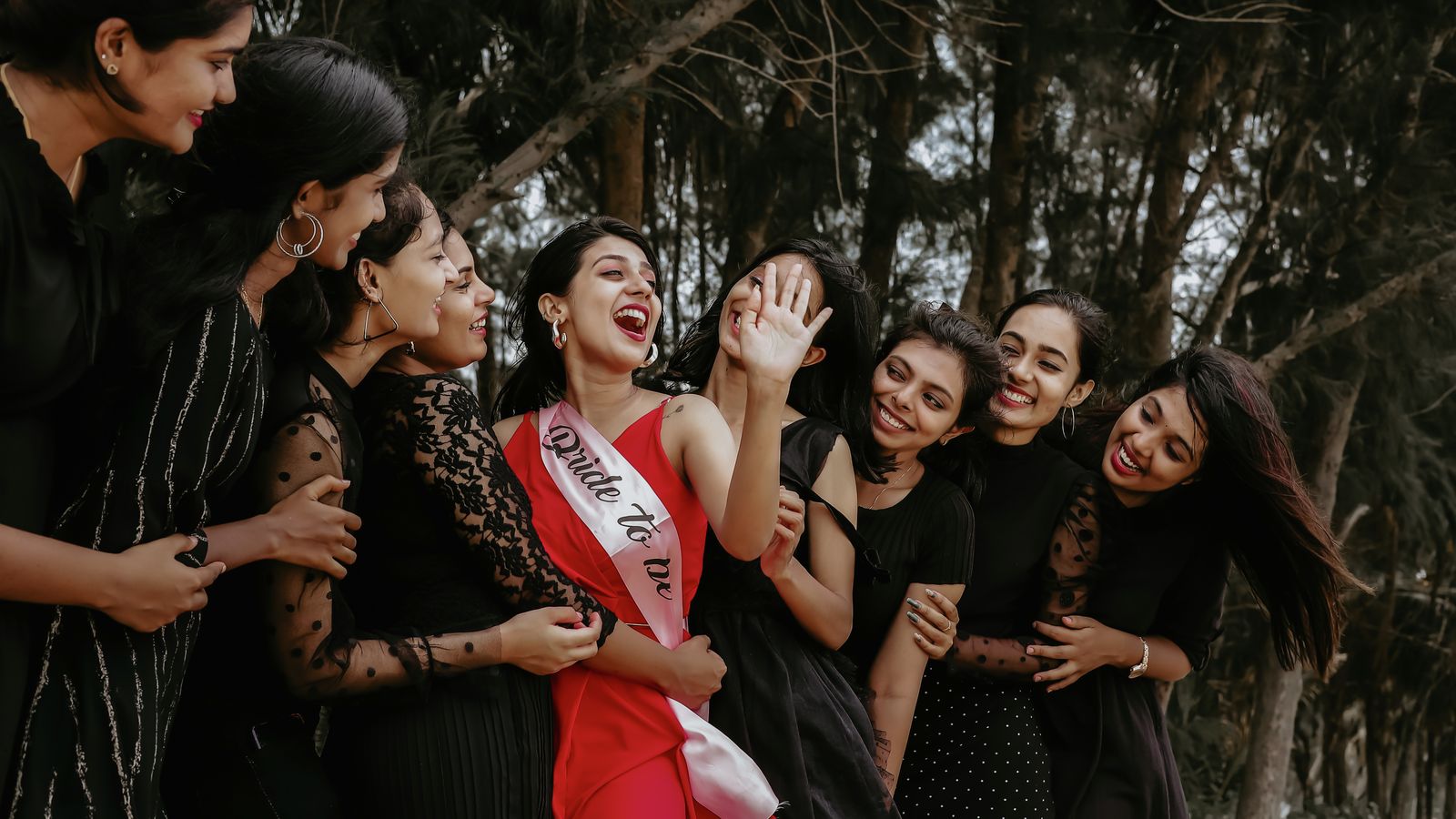 A group of women joyously celebrating outdoors with the bride-to-be wearing a sash.
